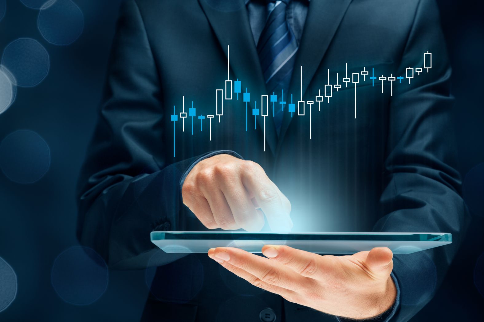 A businessman using a digital tablet with a glowing financial chart and candlestick graph rising upward, representing investor analysis and market growth.